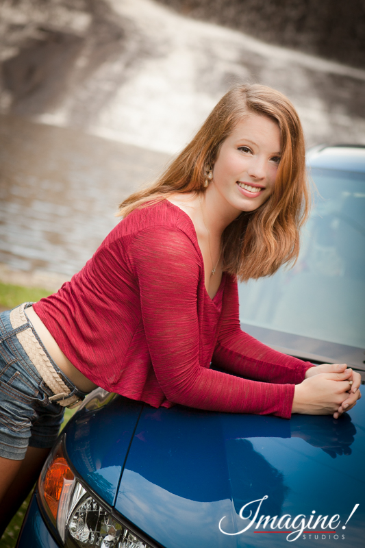 Bethany relaxes against her car in front of a waterfall during her senior model outdoor photo session at Highland Lake Inn in Flat Rock, NC