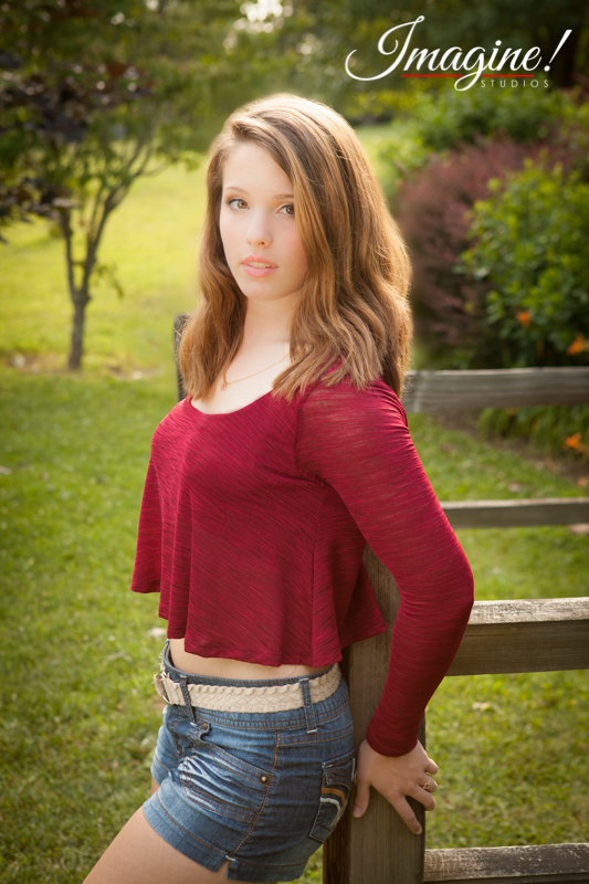Bethany poses against a fence during her senior model outdoor photo session at Highland Lake Inn in Flat Rock, NC