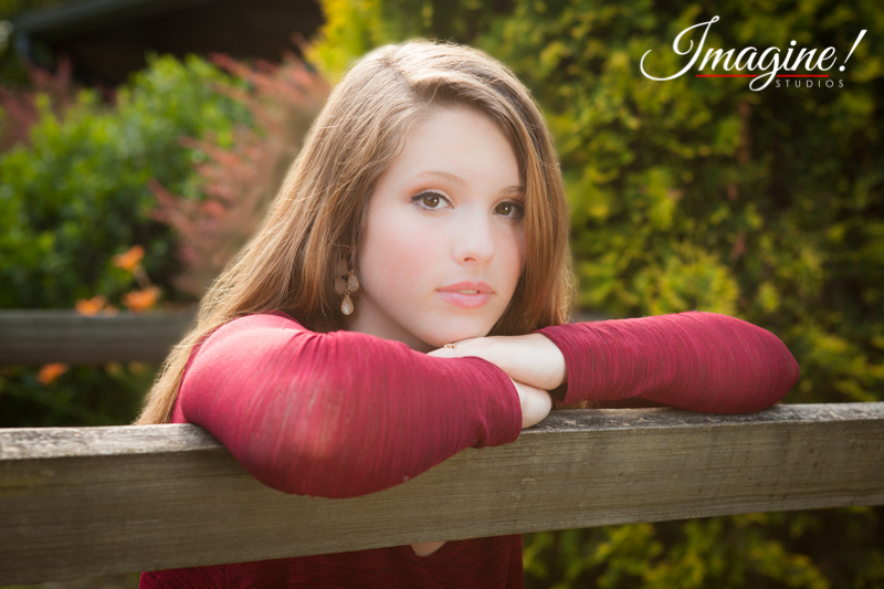 Bethany relaxes against a fence during her senior model outdoor photo session at Highland Lake Inn in Flat Rock, NC