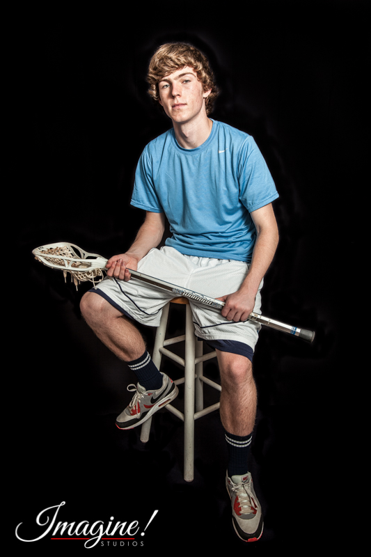 Matthew sits on a stool with his lacrosse stick in his lap